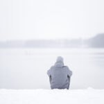 Mann sitzt im Schnee am See