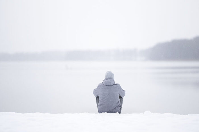 Mann sitzt im Schnee am See
